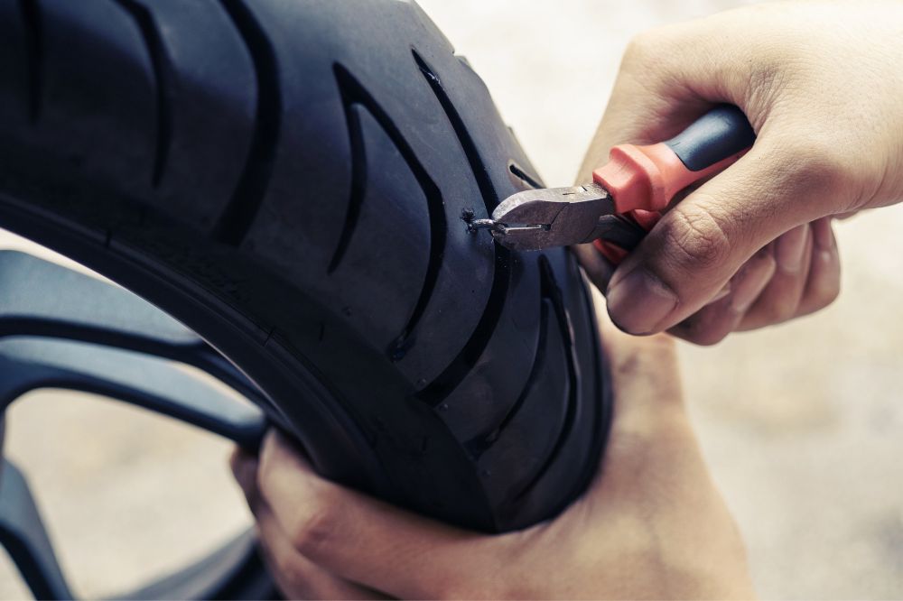 Muž vytahuje kleštěmi hřebík z motocyklové pneumatiky