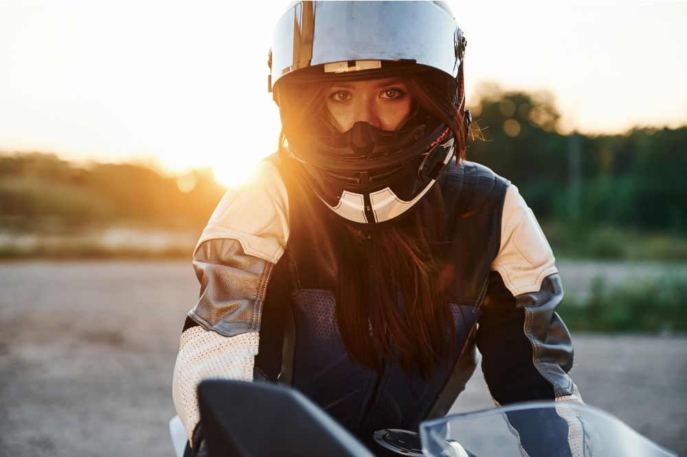 Žena s moto přilbou a koženou bundou sedí na motorce