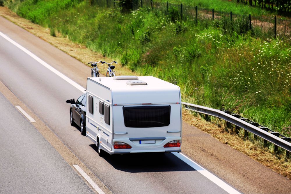 Auto jede po silnici s koly na stře&scaron;e a př&iacute;věsn&yacute;m karavanem