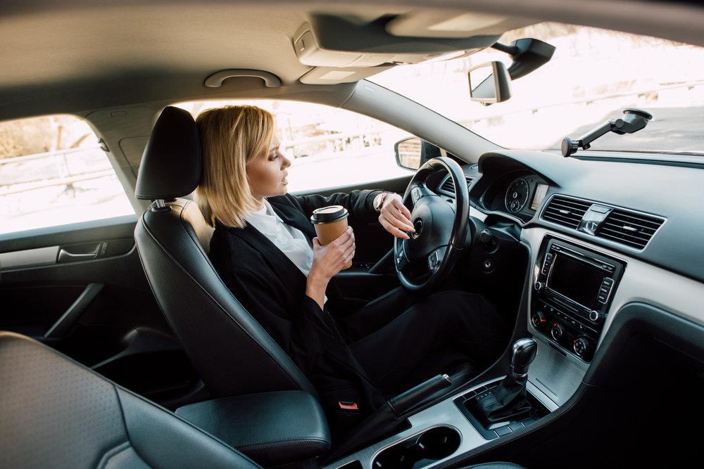 Žena s kávou v ruce za volantem 