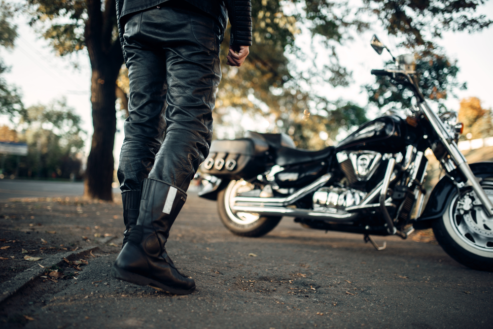 Černé motorkářské boty, kalhoty a motorka v pozadí