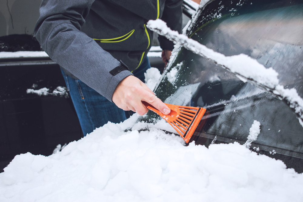 Muž seškrabuje sníh a led ze skla auta