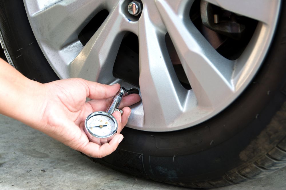 Řidič kontroluje tlak v pneumatice pomocí měřiče tlaku